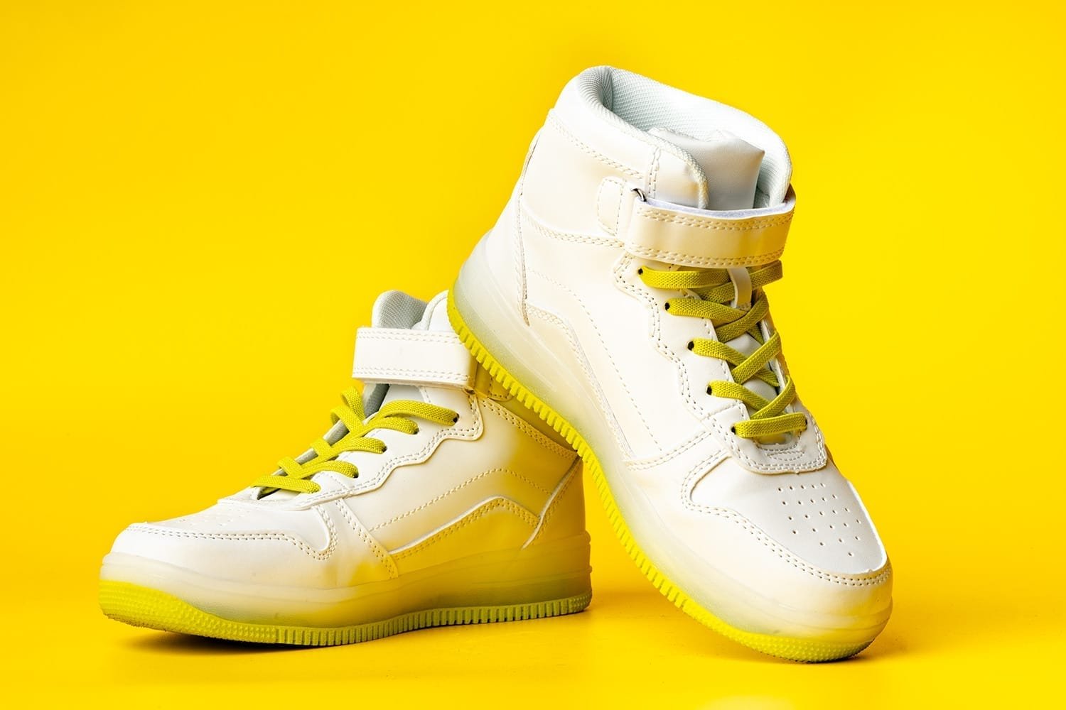 White sneakers with yellow neon laces on yellow background